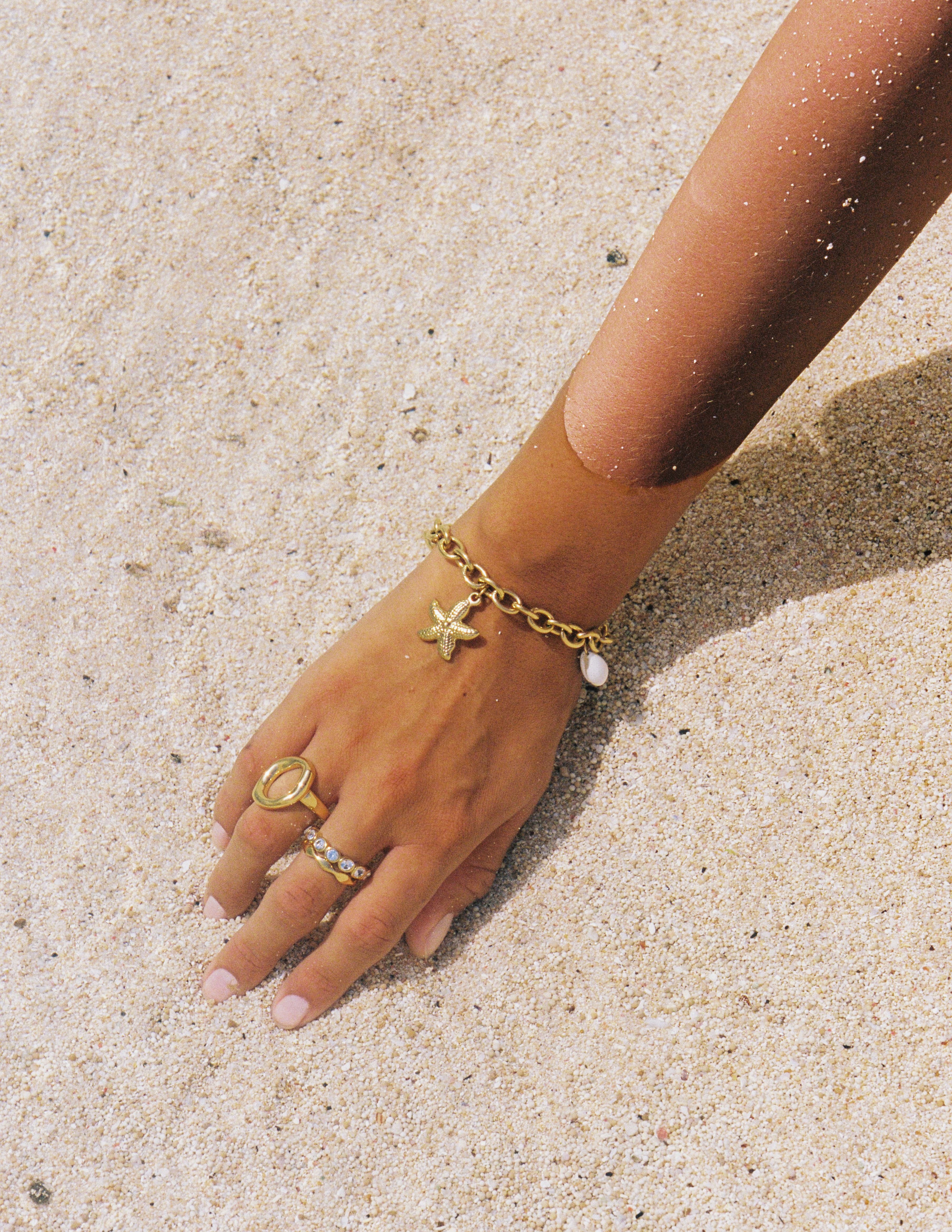 1 year anniversary gifts for girlfriend jewelry featuring a starfish bracelet, gold circle ring and stacking rings styled on a sandy beach