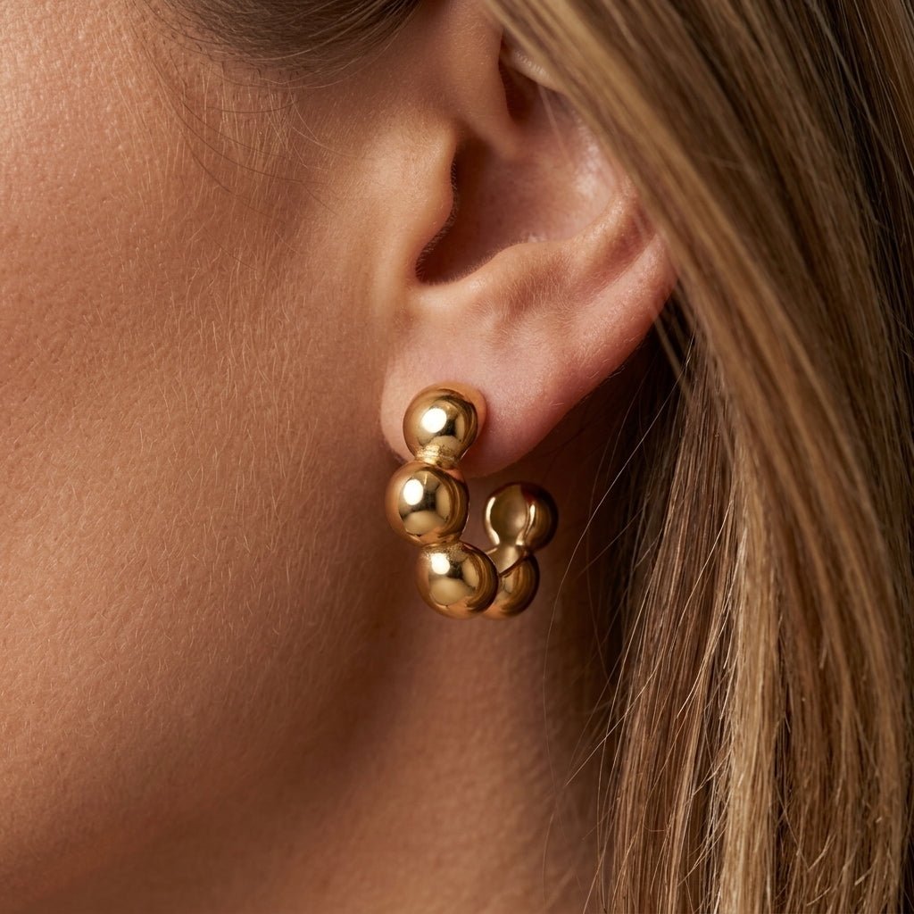 bubble hoop earrings, chunky gold bubble huggie earrings worn on ear, polished gold ball hoop earrings for women, bold sculptural statement jewelry with a modern aesthetic