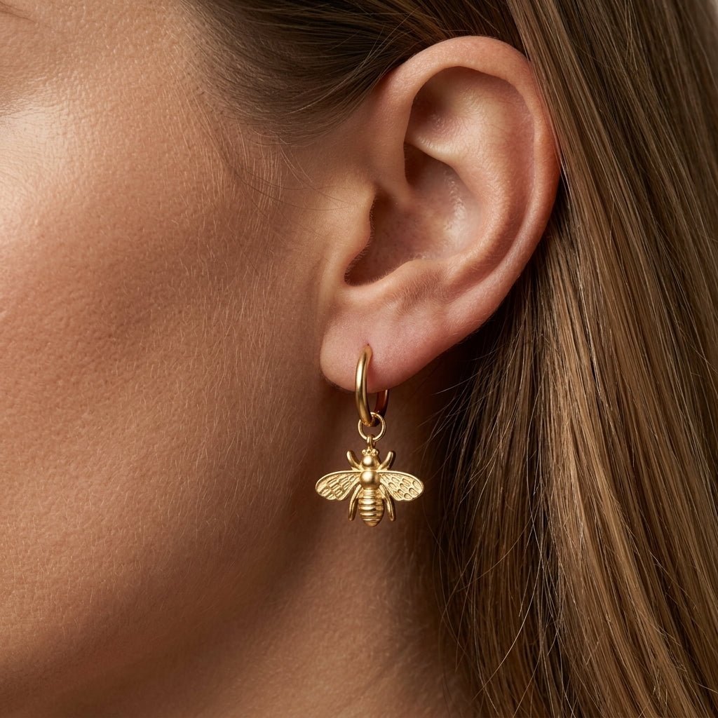 gold bumble bee charm hoop earrings worn on ear, minimalist dainty bee jewelry for women, small gold bee drop earrings with detailed wings, luxury nature-inspired fashion accessory