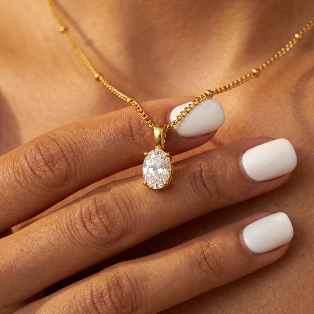 dainty gold cubic zirconia pendant necklace with a sparkling oval solitaire stone styled on a model with white manicured nails