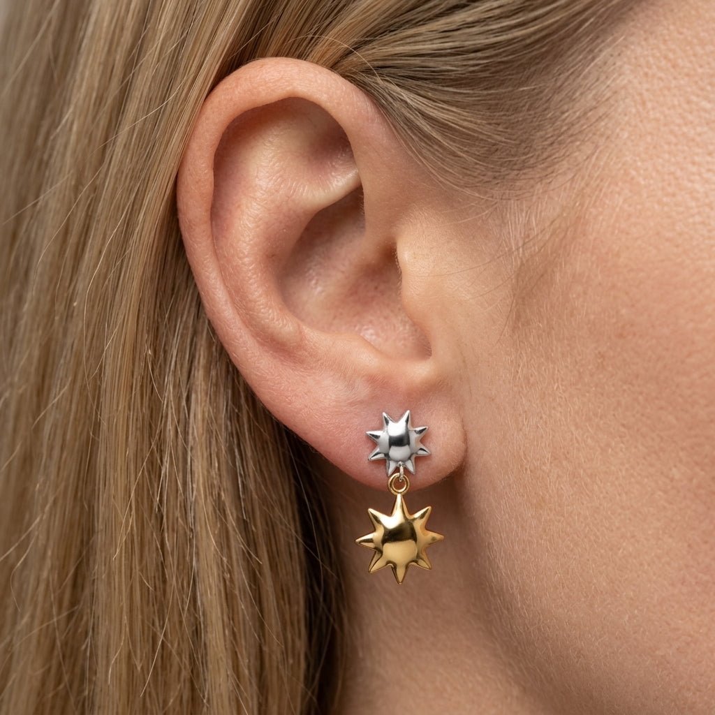 double star gold earrings mixed metal star drop earrings with silver and gold celestial charms styled on pierced ear for a playful look