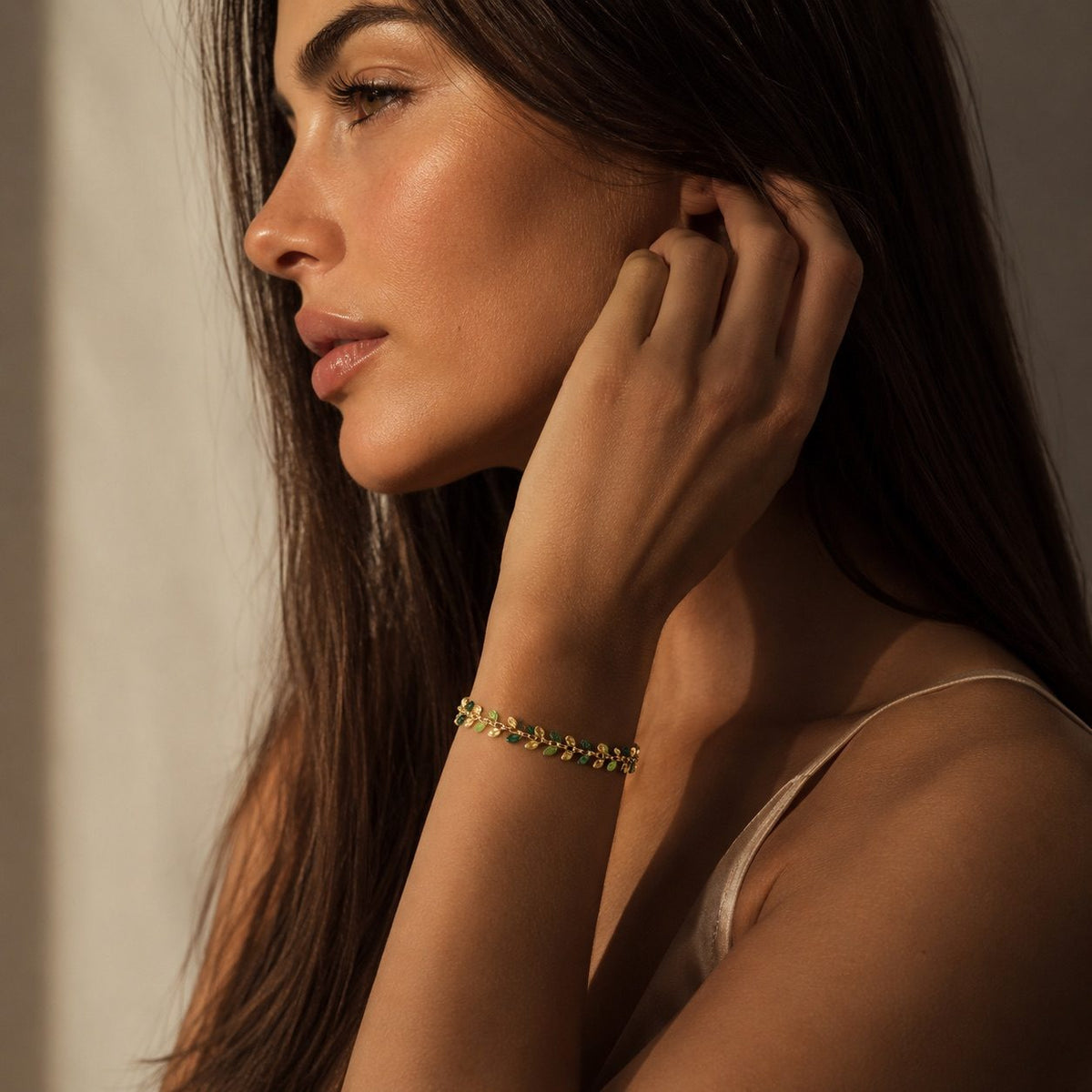 gold botanical leaf bracelet with green foliage-inspired details styled on the wrist by the ocean