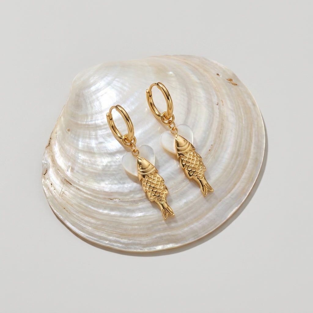 gold fish earrings, ocean themed earrings and beach earrings with detailed gold fish charms and pearl effect accents, coastal inspired hoop jewelry styled on a natural shell background