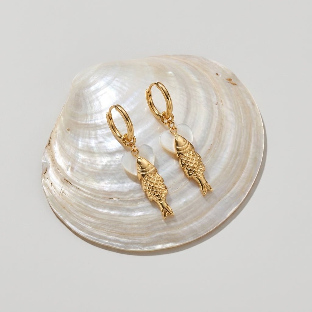 gold fish earrings, ocean themed earrings and beach earrings with detailed gold fish charms and pearl effect accents, coastal inspired hoop jewelry styled on a natural shell background