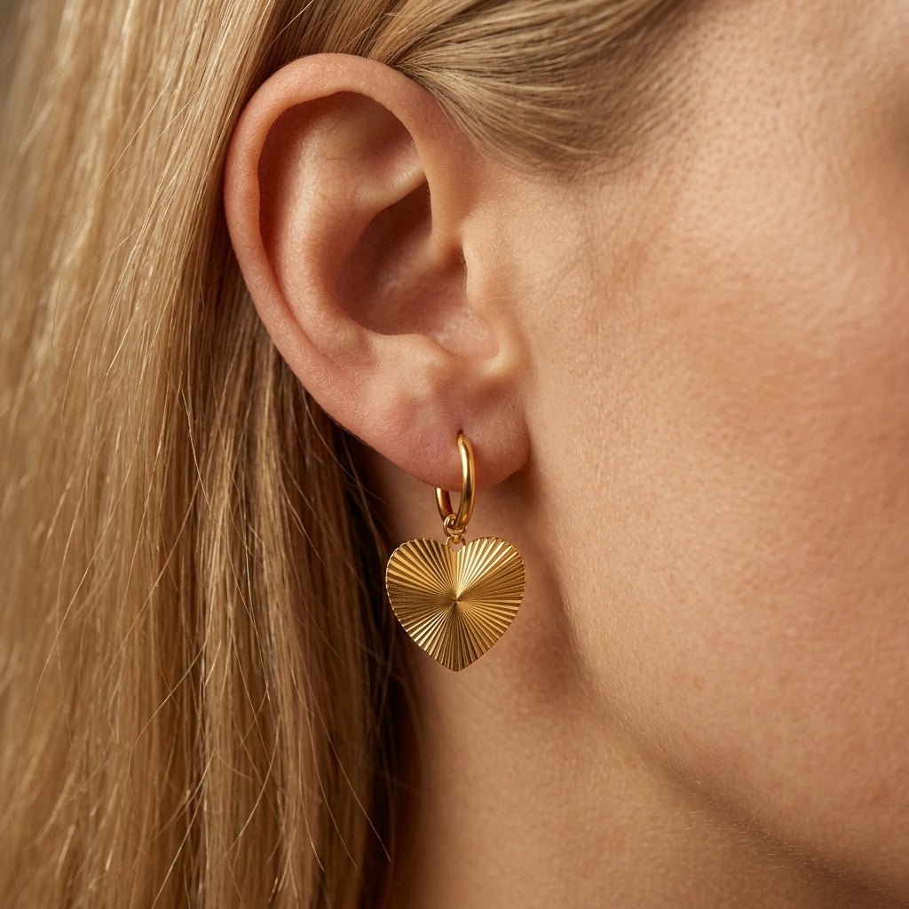 heart drop earrings elegant gold heart drop earrings featuring textured sunburst heart charms suspended from delicate gold huggie hoops, worn on a woman’s ear with a minimal luxury jewelry aesthetic perfect for everyday wear, gifting, layering and modern romantic styling