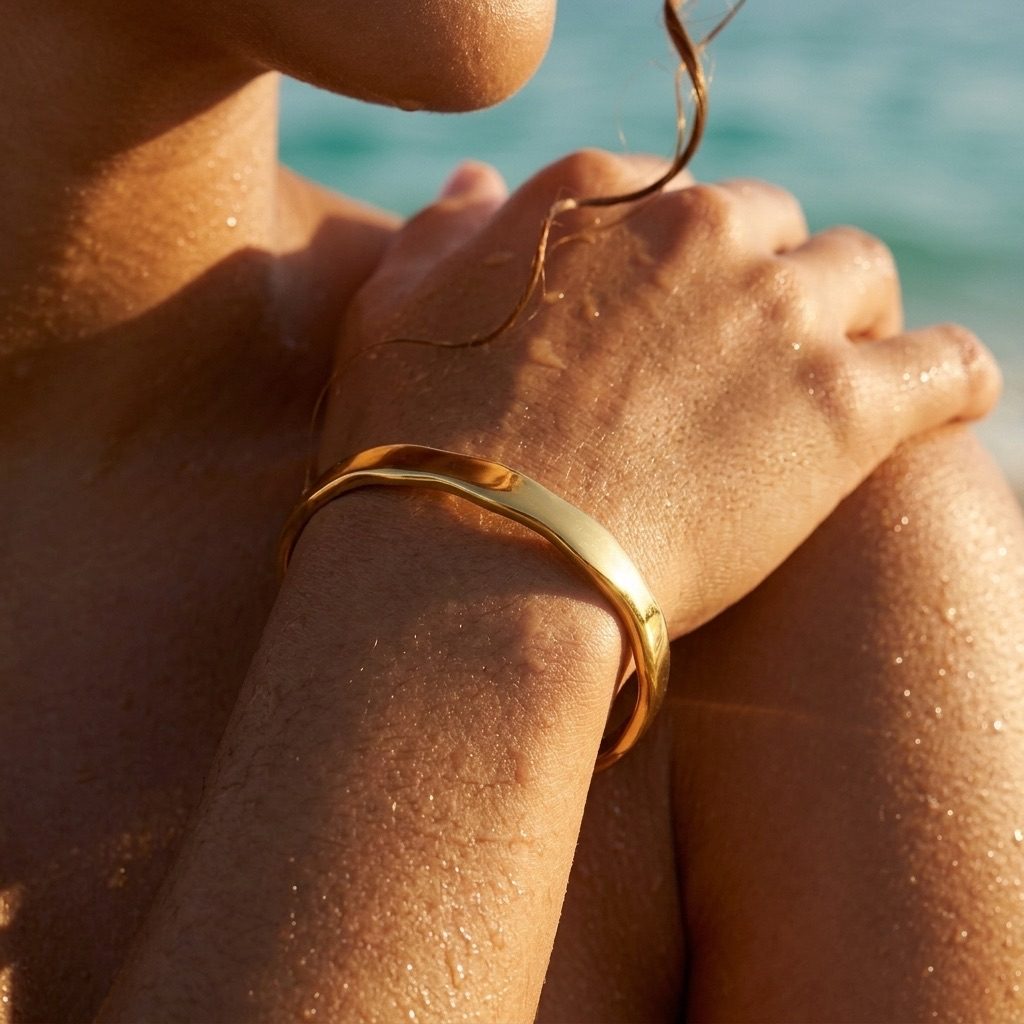 gold wave cuff bracelet with a fluid curved silhouette styled on the wrist in a sunny beach setting