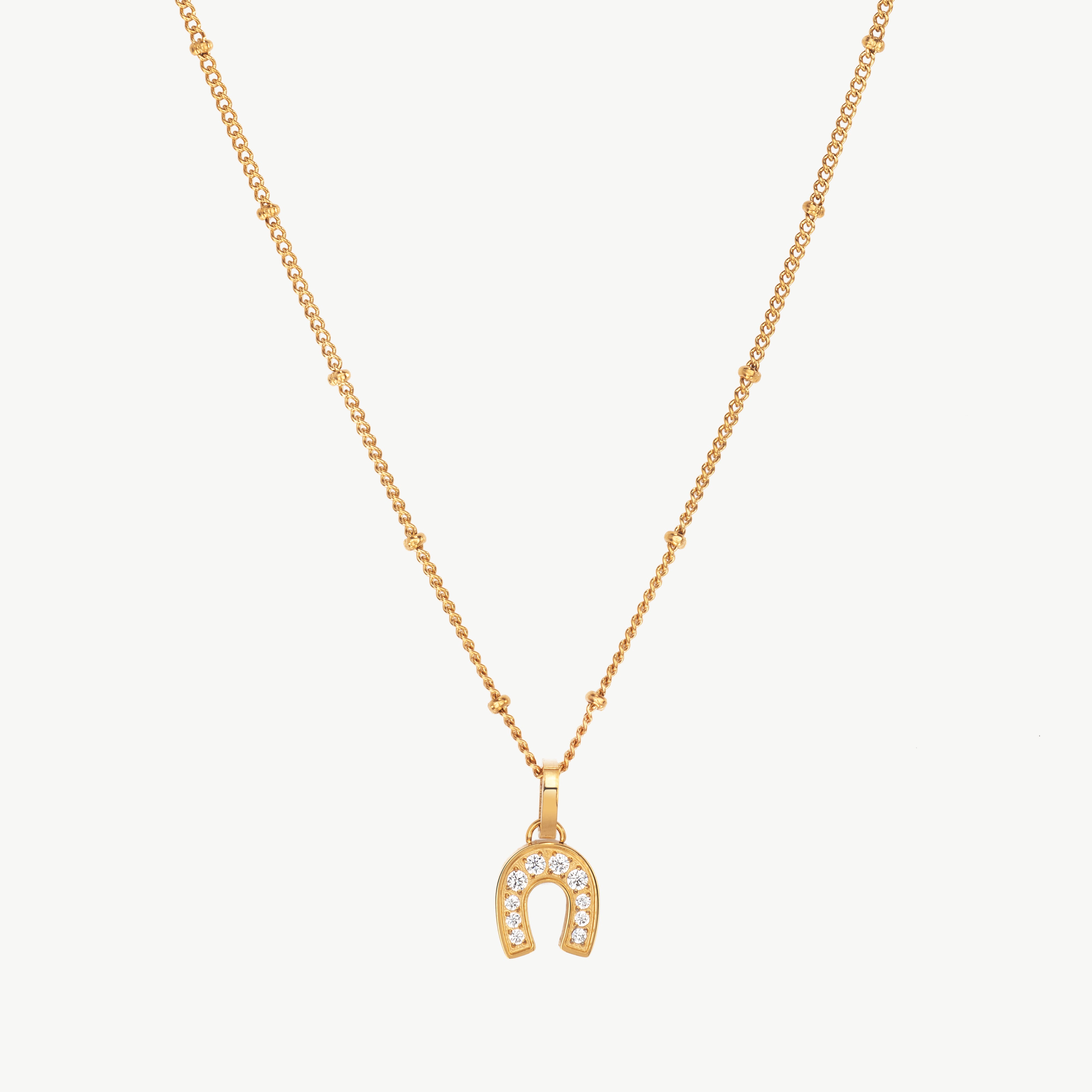 horseshoe charm necklace in gold with small curved pendant, gold horseshoe charm necklace and horseshoe pendant necklace forming a delicate lucky detail