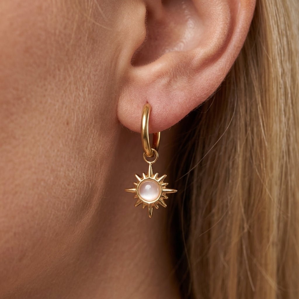 star earrings elegant gold star drop earrings featuring a radiant sunburst charm with a luminous pearl centre suspended from delicate gold huggie hoops, worn on a woman’s ear with a celestial luxury jewellery aesthetic perfect for everyday wear, gifting, layering and modern boho styling