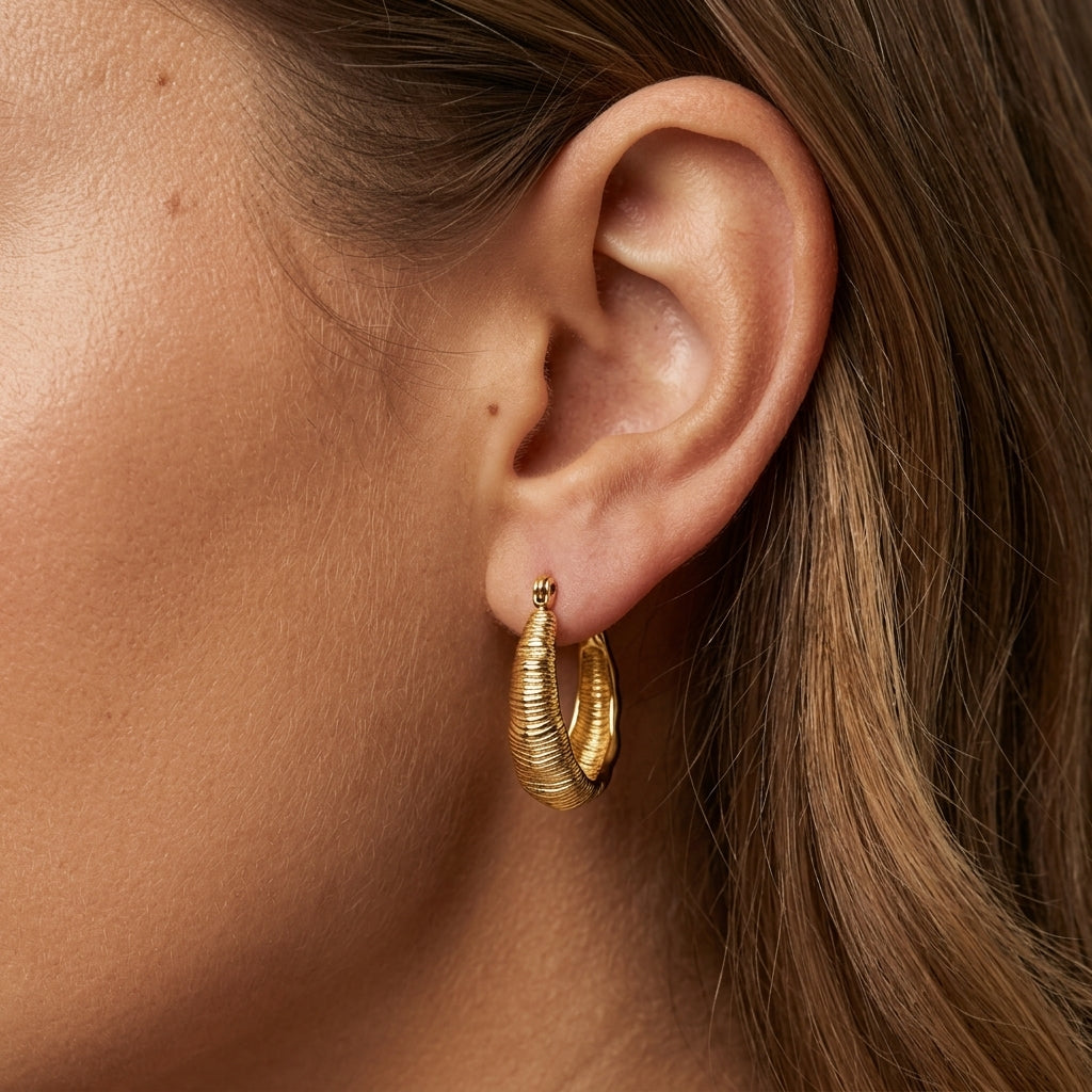 statement gold dome earrings featuring wide curved hoops with a ribbed textured surface and sculptural design displayed on a white background