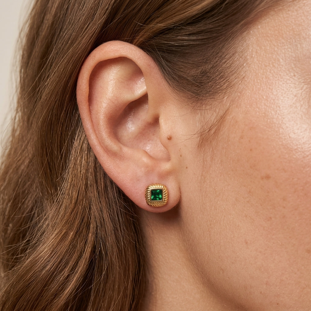 stud green earrings, gold square stud earrings worn on ear with emerald green gemstone center, vintage inspired statement jewelry with textured gold detailing and an elegant retro aesthetic