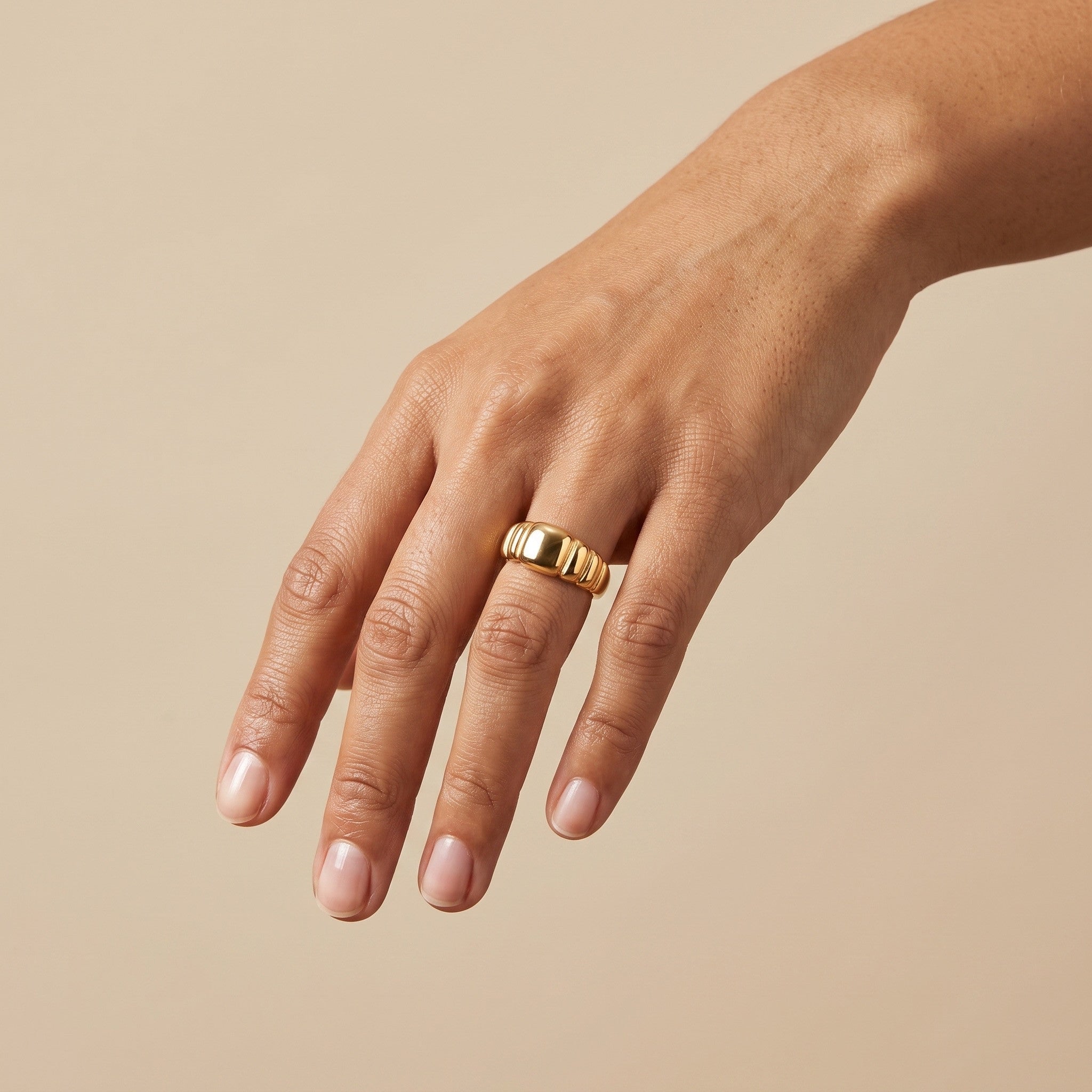 bold gold signet ring with a polished center and ridged band, worn on hand