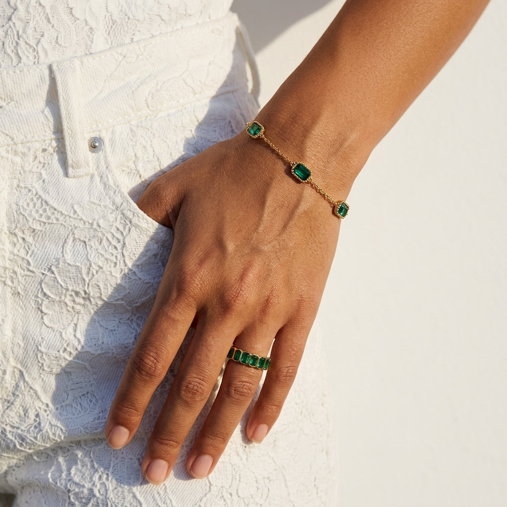 emerald green crystal bracelet featuring sparkling green stones framed by textured gold edges worn on a woman's wrist with a white lace dress