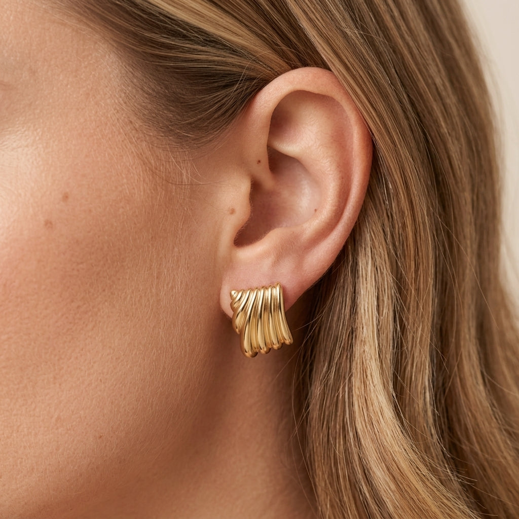 sculptural gold earrings featuring a bold square inspired design with flowing curved ridges and a shiny gold finish styled on a model 