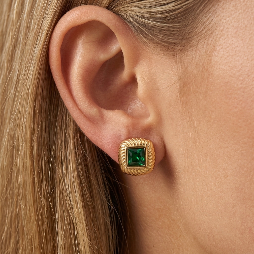 stud green earrings, gold square stud earrings worn on ear with emerald green gemstone center, vintage inspired statement jewelry with textured gold detailing and an elegant retro aesthetic